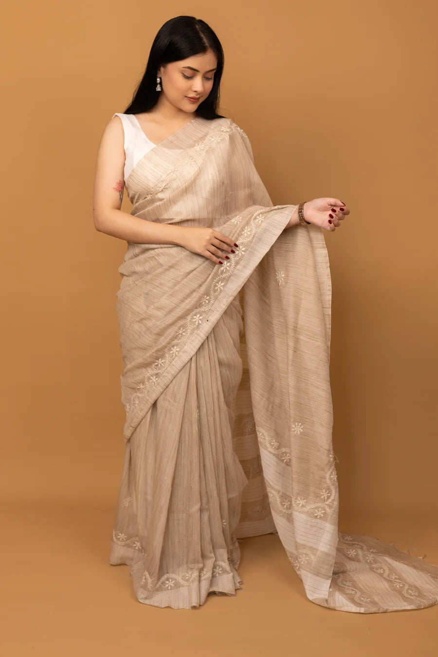Woman wearing a beige saree with a plain background