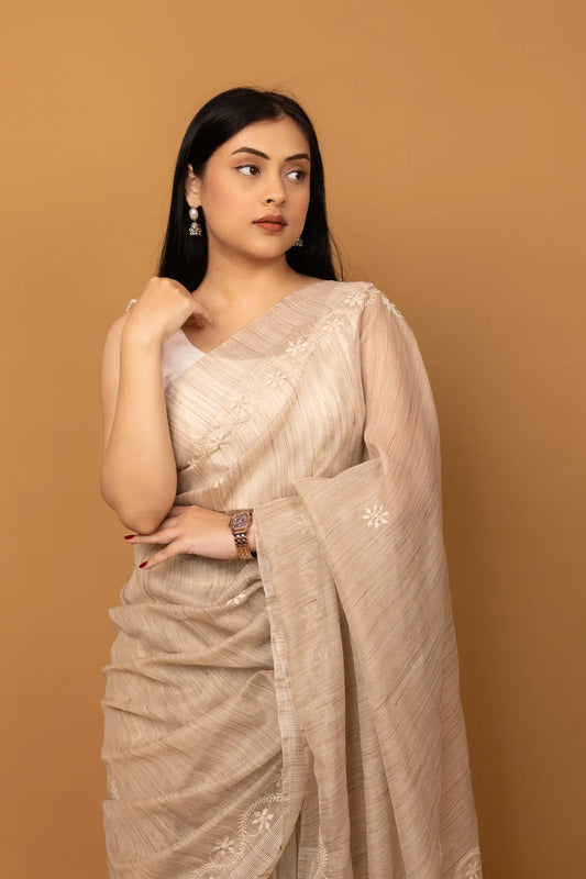 Woman wearing a beige saree with a plain background