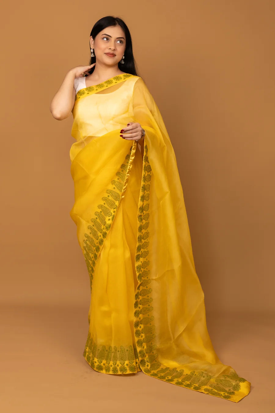 Woman wearing a yellow saree with green border on a brown background